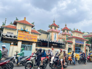 寺の前を走るバイクの写真。ベトナム・ホーチミンのローカル市場を散歩。